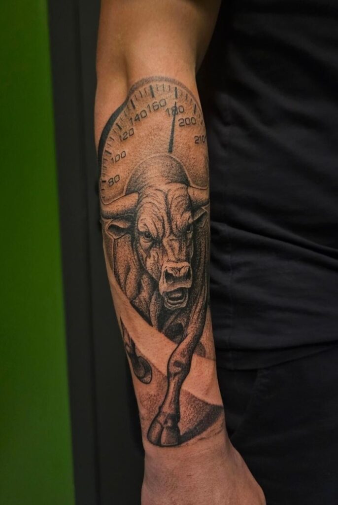 A detailed black and grey realism tattoo on a forearm by Bryan of Mutant Ink. The design features a powerful bull charging forward, set against the backdrop of a large speedometer dial showing high speeds.