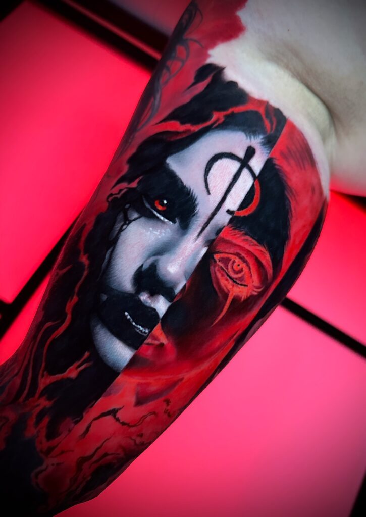 A high-contrast black and red realism tattoo by Kenny of Hannon Tattoo. The design shows a face split vertically, with one side featuring a glowing red eye and a mystical symbol on the forehead.