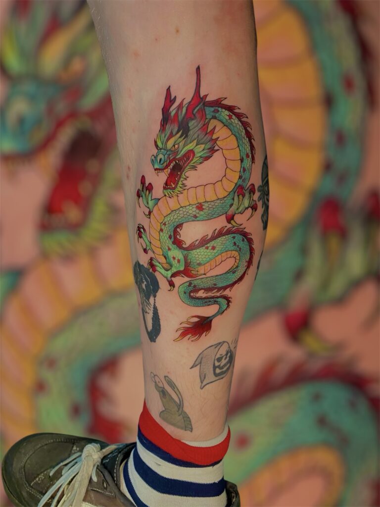 A colorful teal and red dragon winding vertically on a calf, an intricate illustrative piece by artist Lavinja of LesDix Noirs.