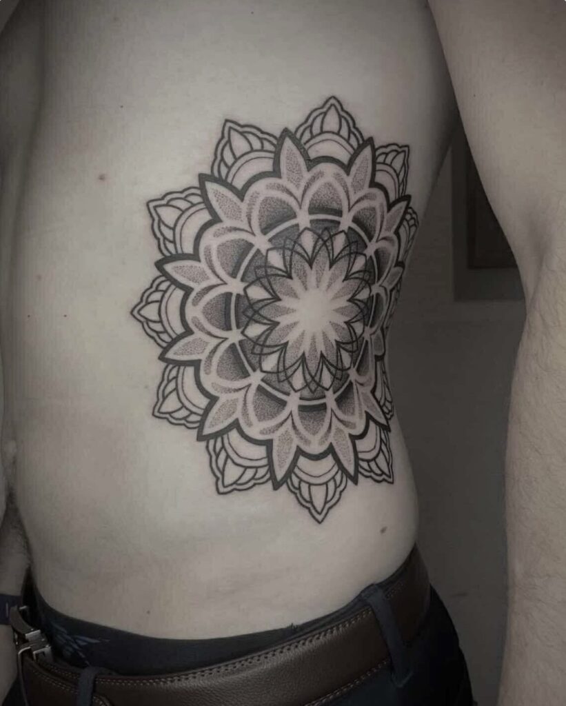 A detailed black-ink mandala tattoo placed on a person's ribs by Emmi from Pink Flamingo. The design showcases precise linework and soft shading to create a striking, circular geometric piece.