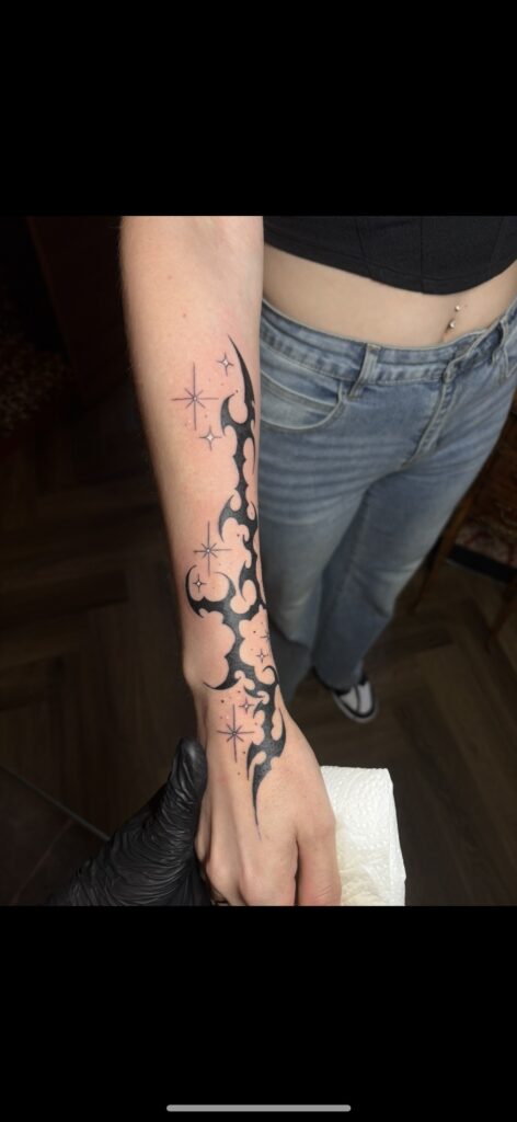 A sharp, black-ink "cyber-sigilism" style tattoo on a forearm by Delfien of Trick or Tat, featuring abstract, fluid lines combined with delicate four-pointed stars.