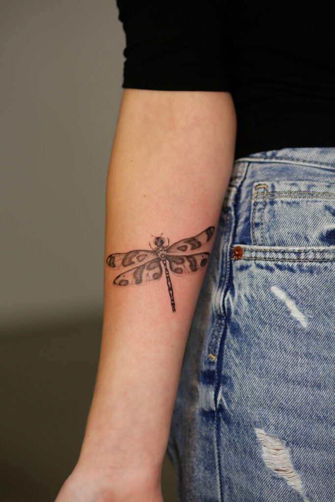 A delicate and symmetrical dragonfly tattoo on an inner forearm, featuring fine linework and soft shading on the wings.