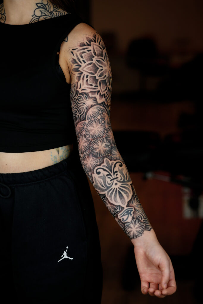 Een volledige arm-sleeve met in elkaar grijpende geometrische mandala's en "Flower of Life"-patronen, uitgevoerd in contrastrijk zwart en dotwork door Bence van BenHTattoo.