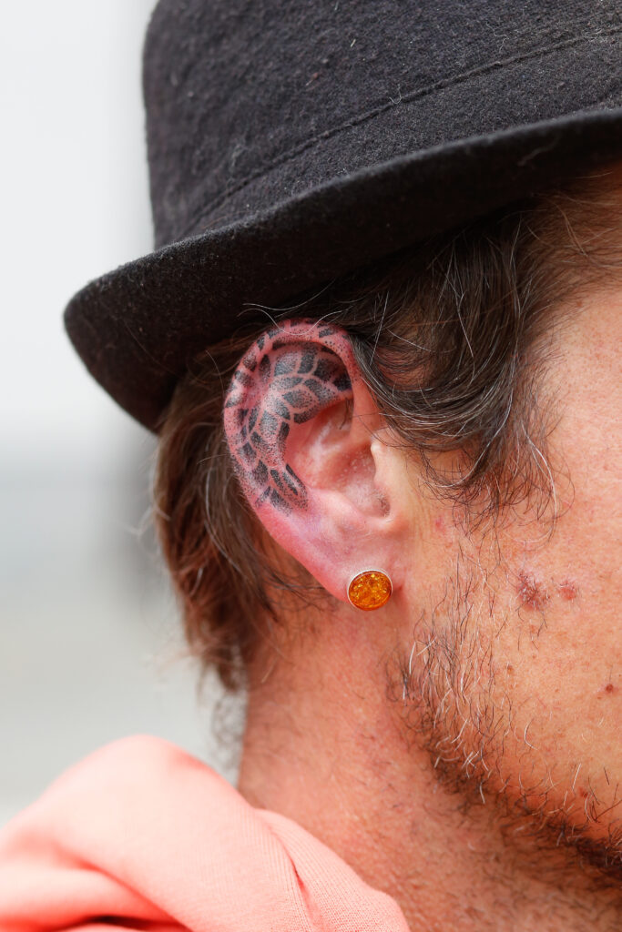 Een close-up van een unieke tatoeage in het oor, waarbij de oorschelp en helix zijn versierd met fijne zwarte bloem- en geometrische patronen in dotwork-stijl door Bence van BenHTattoo.