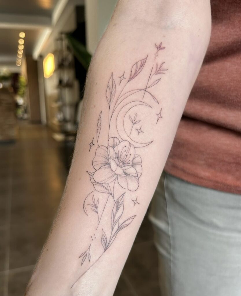 A delicate and elegant fineline tattoo on a forearm, created by Christa from Obscuria Gratia. The design depicts a soft, detailed flower intertwined with a slender crescent moon and small, twinkling four-pointed stars.