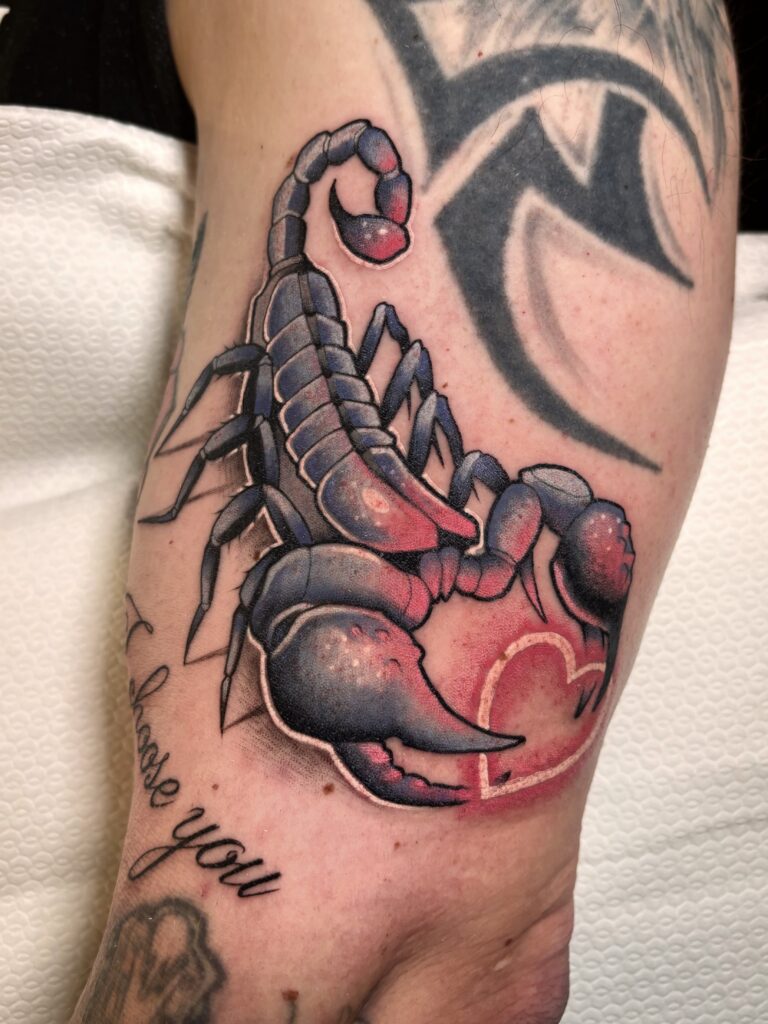 A detailed color tattoo of a scorpion by Sabbe of T-paint/Roxy. The scorpion is rendered in dark blue and purple with bright pink highlights, and one of its claws is holding a glowing pink heart outline. The script "I choose you" is visible below.