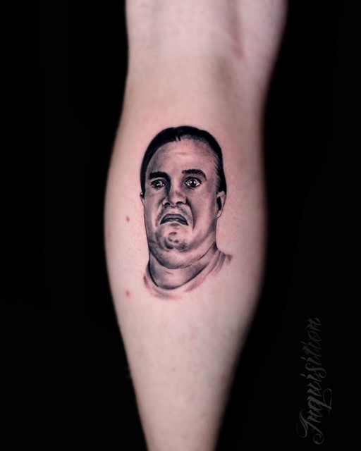A detailed black and grey realism tattoo on a limb by Gianni from Inquisition Tattoo. It depicts a portrait of a man's face with a wide-eyed, shocked, or frightened expression, rendered with smooth shading and fine detail.