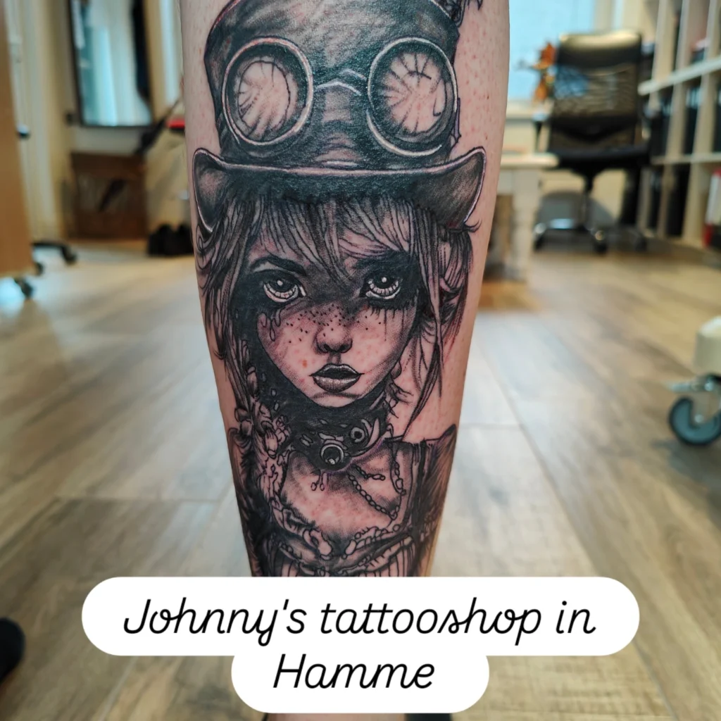 Een gedetailleerde black and grey tattoo op een arm van een meisje met sproetjes in steampunk-stijl, inclusief een hoge hoed met goggles en mechanische details. De tattoo toont fijn schaduwwerk en karakteristieke lijnen. Gezet door Johnny van Johnny's Tattoos Hamme tijdens de Sint-Niklaas Tattoo Expo.