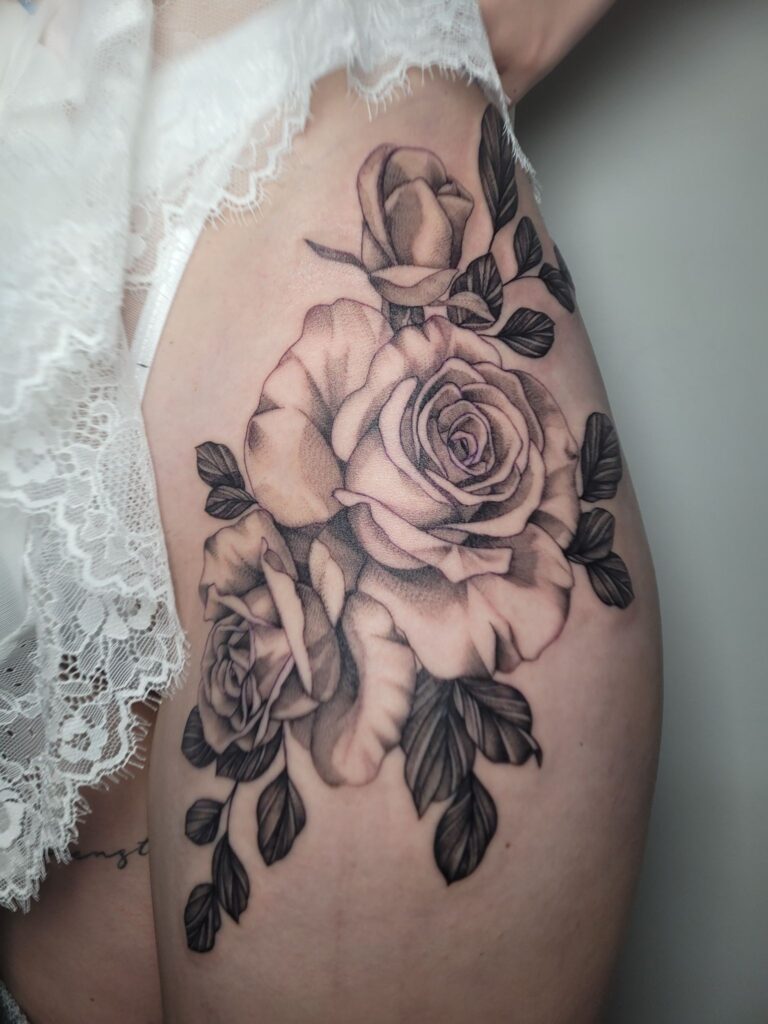 "Een elegante fine-line tattoo van een boeket rozen op de heup en het bovenbeen. De tattoo kenmerkt zich door zachte schaduwen en gedetailleerde bladeren in black and grey stijl. Gezet door Ellen van Black Swan Tattoo op de Sint-Niklaas Tattoo Expo.
