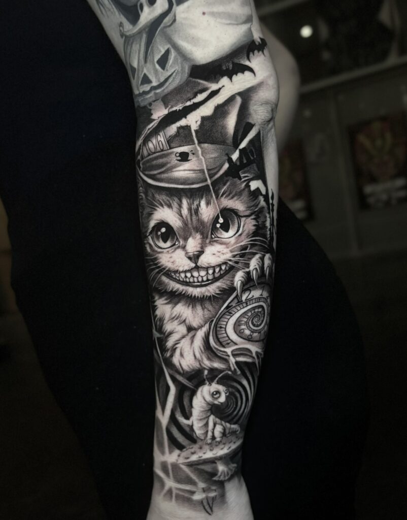 Een indrukwekkende black and grey arm-sleeve geïnspireerd door Alice in Wonderland. Centraal staat de breed grijnzende Cheshire Cat met uiterst gedetailleerde vacht, geflankeerd door de rups op een paddenstoel, een zakhorloge en een vliegende pompoen bovenaan. Werk van Dante (Dante Ink) op de Sint-Niklaas Tattoo Expo.