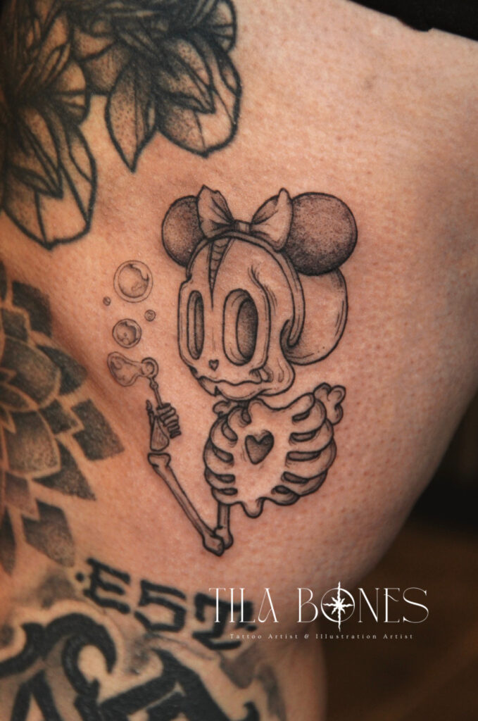 Een creatieve zwart-wit tattoo van een muizen-skelet met een strikje, dat bellen blaast. Het ontwerp is gezet in een fijne illustratieve stijl met subtiele schaduwen. Werk van Phoebe (Tila Bones) op de Sint-Niklaas Tattoo Expo.