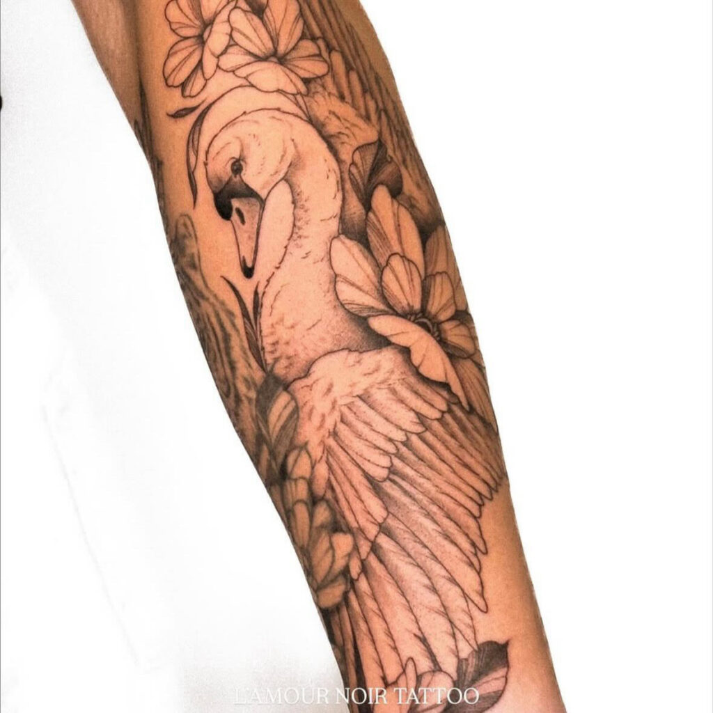 Een grootschalige tattoo op een arm van een sierlijke zwaan omringd door grote bloemen. Het ontwerp combineert strakke outlines met zacht schaduwwerk, waarbij de witte veren van de zwaan prachtig contrasteren met de donkere achtergrond. Werk van Chelsy (L'amour Noir Tattoo) tijdens de Sint-Niklaas Tattoo Expo.