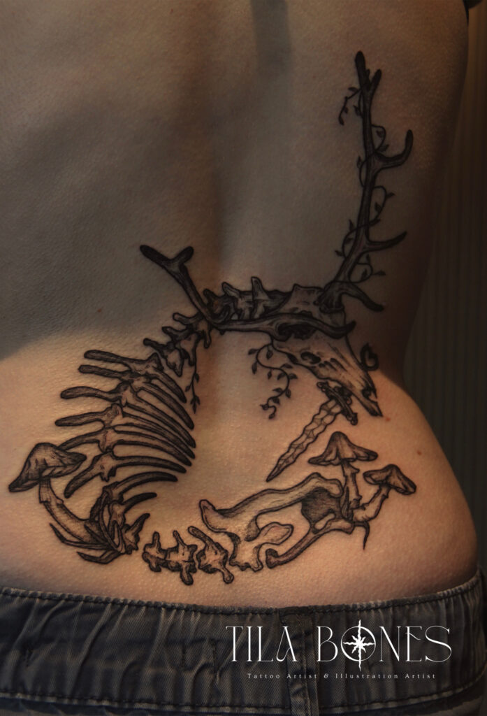 Een gedetailleerde rugtattoo van een dierlijk skelet (hertachtig) omringd door paddenstoelen en klimop. De compositie volgt de natuurlijke lijnen van de onderrug. Gezet door Phoebe van Tila Bones tijdens de Sint-Niklaas Tattoo Expo.