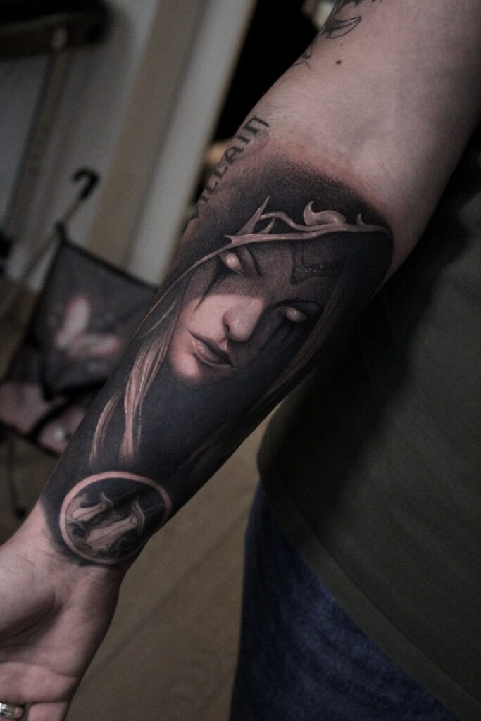 Een hyperrealistische black and grey tattoo van Sylvanas Windrunner uit World of Warcraft op een onderarm. De tattoo toont de Banshee Queen met haar kenmerkende helm, gloeiende ogen en tranen op haar wangen, uitgevoerd met extreem fijn schaduwwerk. Werk van Jana (Jana Jacques Tattoo) op de Sint-Niklaas Tattoo Expo.