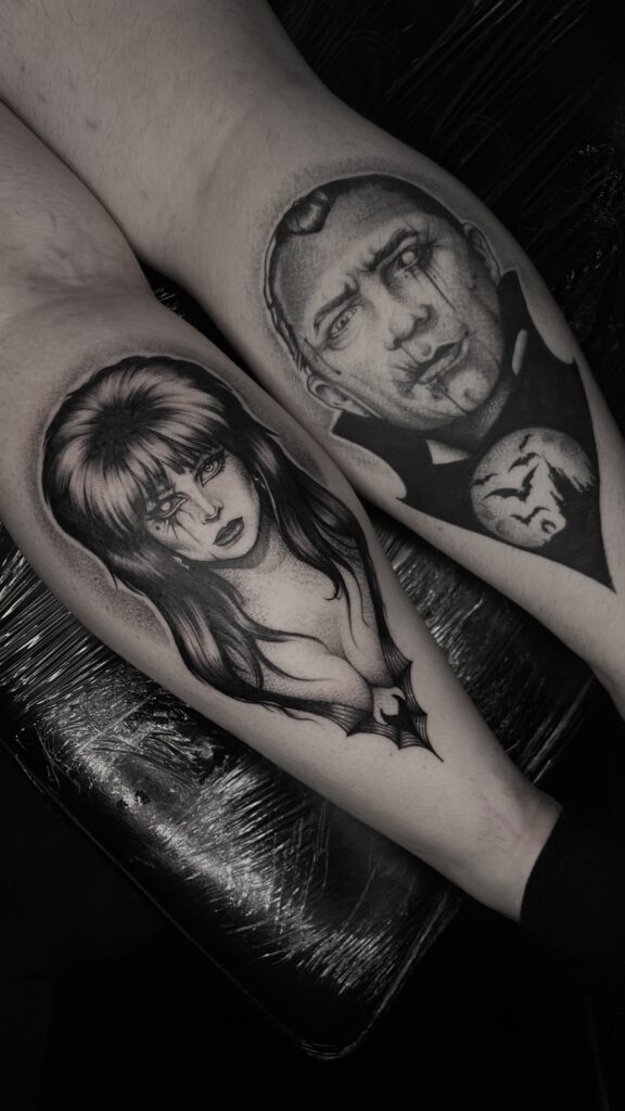 Twee gedetailleerde black and grey portretten op aangrenzende lichaamsdelen. Links het iconische portret van Elvira, Mistress of the Dark, met haar kenmerkende haar en vleermuisdetails. Rechts een sinister portret van Dracula met tranende ogen en een vleermuissilhouet voor de volle maan. Gezet door Kim van Transylveinia Tattoo op de Sint-Niklaas Tattoo Expo.
