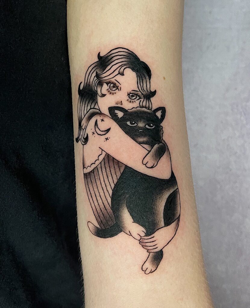 Een charmante blackwork tattoo van een meisje dat een grote zwarte kat stevig omhelst. Het ontwerp bevat subtiele details zoals sterren en een halve maan op de schouder van het meisje. Gezet door Wietske van Tatties Wietske op de Sint-Niklaas Tattoo Expo.