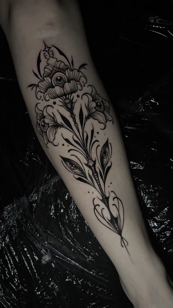 Een unieke en duistere illustratieve tattoo van een bloemachtige vorm waarbij de kelken en bladeren zijn voorzien van realistische, starende ogen. Het ontwerp is uitgevoerd in diepzwart met fijn lijnwerk en dotwork-schaduwen. Werk van Kim (Transylveinia Tattoo) op de Sint-Niklaas Tattoo Expo.