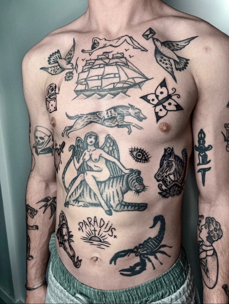 Een overzicht van een torso met verschillende tattoos in een krachtige, traditionele blackwork stijl. De collectie bevat onder andere een groot schip, een gevleugelde vrouw op een tijger, een schorpioen, en diverse kleinere iconen zoals een dobbelsteen en een vlinder. Gezet door Barrie van Black Rain Tattoo op de Sint-Niklaas Tattoo Expo.