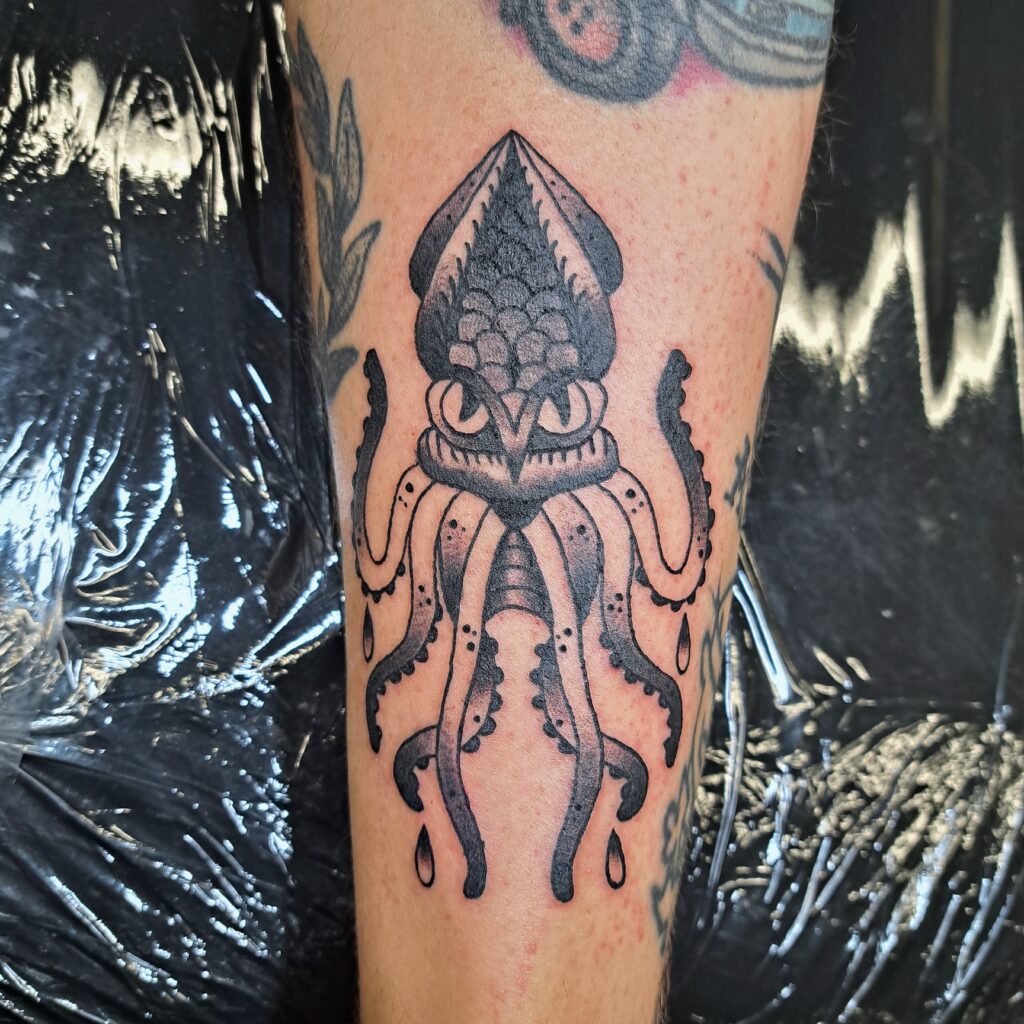Gedetailleerde blackwork tattoo van een inktvis met grote ogen en sierlijke tentakels op een arm. Het ontwerp maakt gebruik van stippeltechnieken voor schaduw en textuur. Gezet door Wietske van Tatties Wietske tijdens de Sint-Niklaas Tattoo Expo.