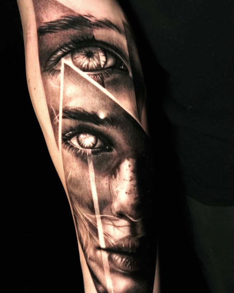 Een indrukwekkende black and grey tattoo op een onderarm die twee realistische ogen toont, gescheiden door scherpe geometrische lijnen. De bovenste helft focust op een enkel oog, terwijl de onderste helft een gedetailleerd gezicht met sproetjes weergeeft. Werk van Nikki Van Trappen op de Sint-Niklaas Tattoo Expo.