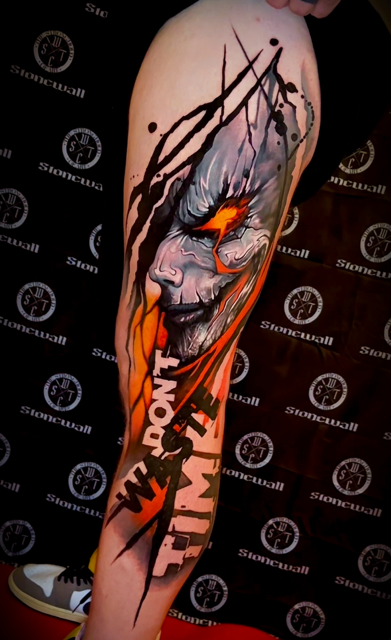 Een opvallende tattoo op een bovenbeen in een moderne, illustratieve stijl. Het toont een vrouwelijk gezicht met gitzwarte ogen en felrode lippen, verweven met abstracte witte lijnen die lijken op barsten of bliksemschichten. De achtergrond bevat dieprode kleurvlakken en geometrische vormen. Gezet door Tom van Oevelen op de Sint-Niklaas Tattoo Expo.