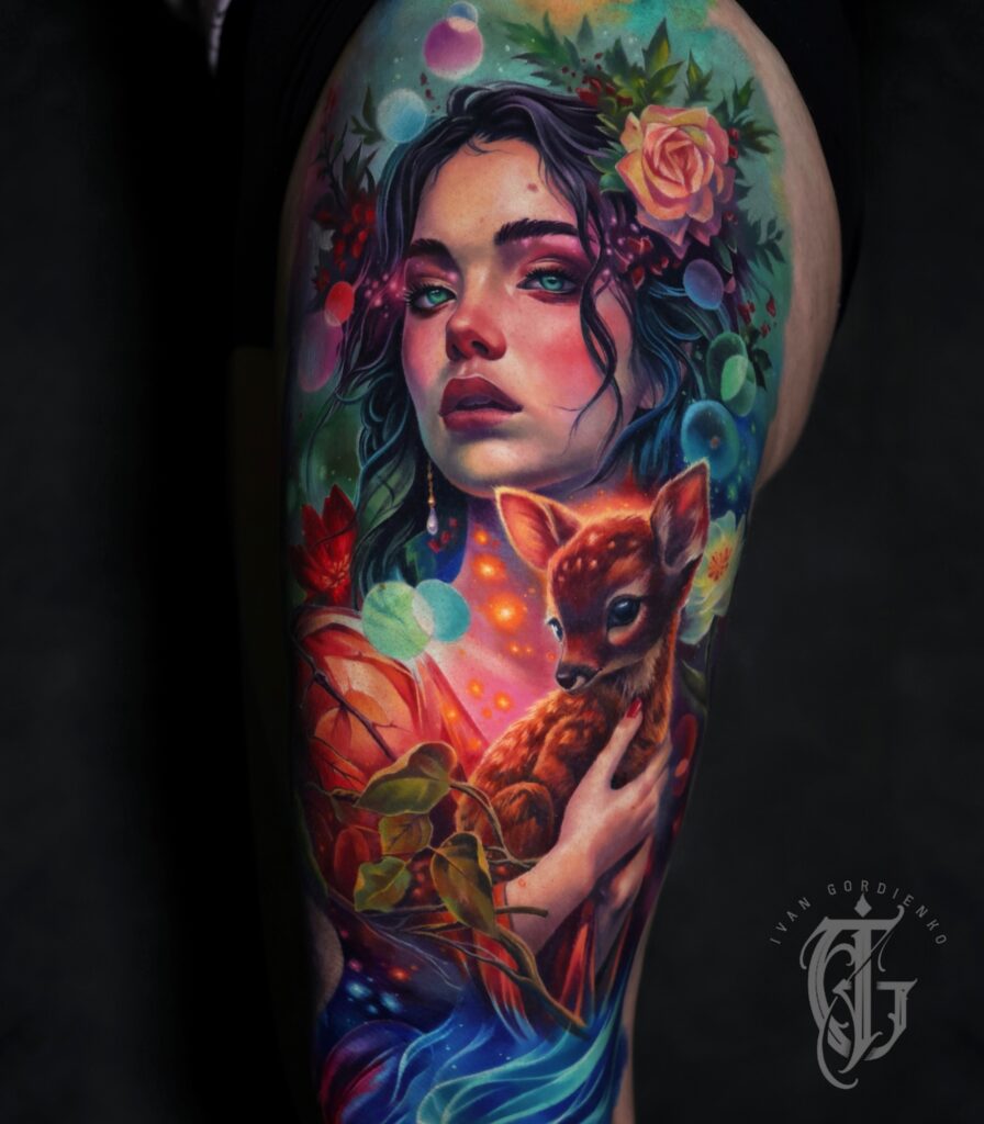 Een adembenemende, dromerige full color tattoo op een bovenbeen. Het toont het portret van een vrouw met diepblauwe ogen en bloemen in haar haar, die teder een klein reekalfje vasthoudt. De compositie is gevuld met magische lichteffecten, bellen en een rijk kleurenpalet van roze, groen en blauw. Vakmanschap van Ivan Gordienko op de Sint-Niklaas Tattoo Expo.